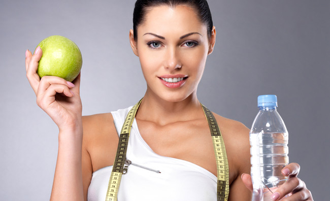Una giovane donna tiene in mano una mela e una bottiglia d'acqua