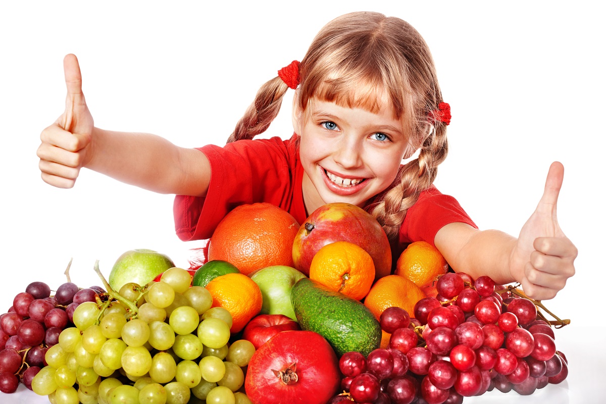 Bambina con un piano pieno di frutta sorride. Pesticidi nei cibi: alimenti europei sicuri il 97%