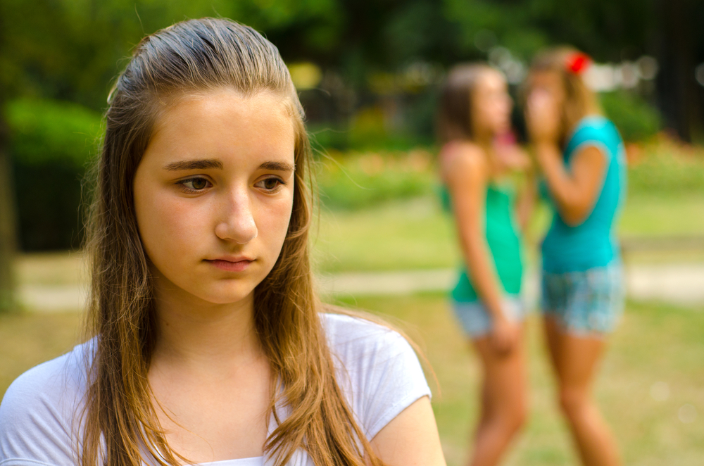 Violenza e abusi, una giovane ragazza cammina con il volto triste e sullo sfondo due ragazze parlano tra loro