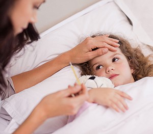 Isindromi simil-influenzali, una bambina a letto mostra sintomi simil influenzali e la madre al suo capezzale le misura la febbre.