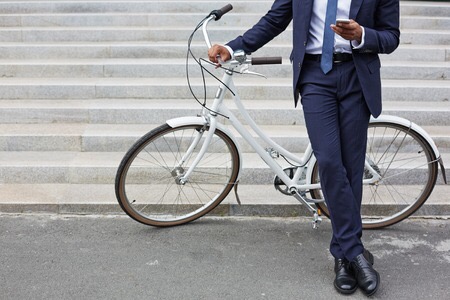 Tumori, un uomo in giacca e cravatta scrive al cellulare appoggiato ad una bici