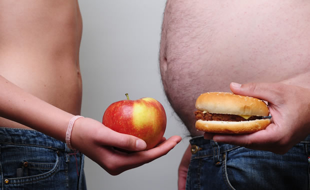 Colesterolo, due uomini tengono in mano un panino e una mela