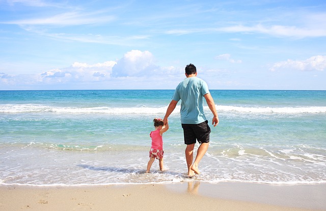 Mare, un papà tiene per mano la figlia e passeggiano sulla spiaggia