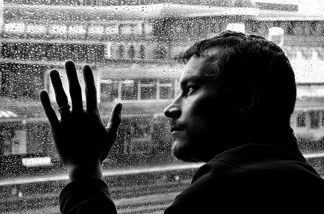 depressione, un uomo in bianco e nero appoggiato su un vetro mentre fuori piove