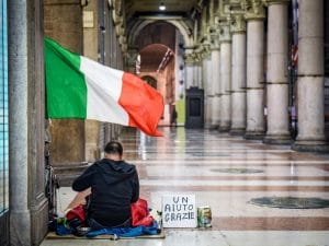 povertà a pasqua. Uomo siede per terra sotto la bandiera italiana