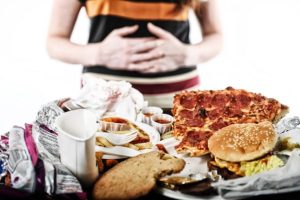 Fibre alimentari, una donna si tocca l'addome e davanti a se una tavola imbandita