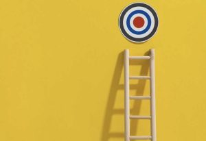 obiettivi, una scala su un muro giallo, con un bersaglio in cima