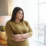 donna con obesità vicino alla finestra con le braccia incrociate
