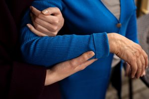 Scompenso cardiaco, le mani di una donna caregiver che sorreggono il braccio di un'anziana