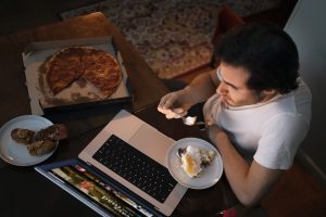 Diabete, un uomo mangia di notte davanti al computer, ha una pizza tagliata a spicchi accanto e un piatto