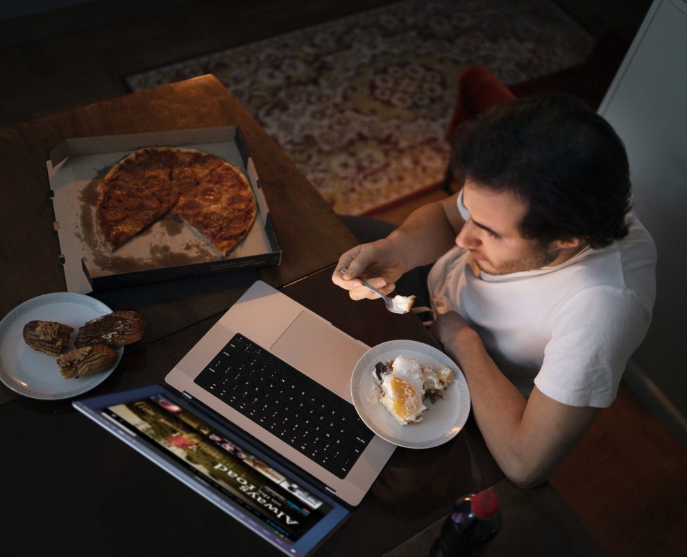 Diabete, un uomo mangia di notte davanti al computer, ha una pizza tagliata a spicchi accanto e un piatto